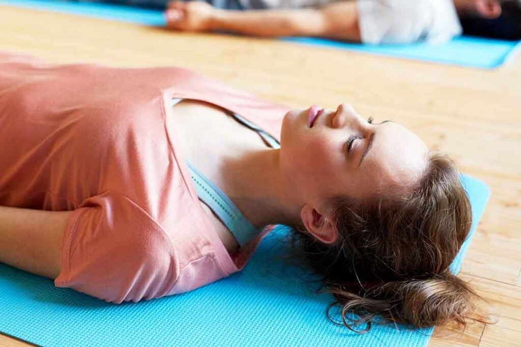 Waarom val ik in slaap tijdens de diepe ontspanning? Vrouw op yogamat in savasana.