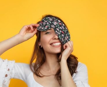 vrouw met oogkussen lachend tegen gele achtergrond.