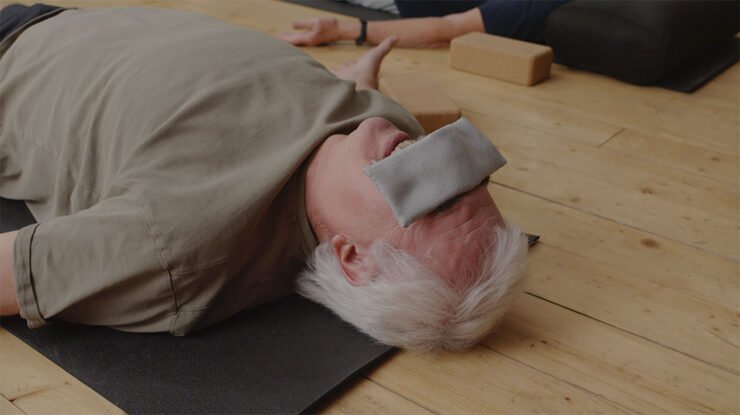 man met oogkussen tijdens meditatie op grond van yogastudio. Verwarmde Oogmaskers: Ontspanning of Risico's?