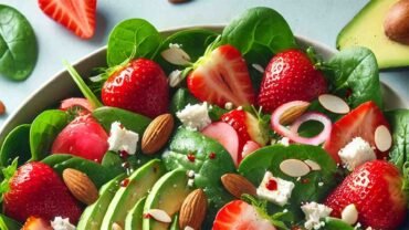 A vibrant and healthy strawberry spinach salad served in a large white bowl. The salad includes fresh baby spinach leaves, sliced strawberries, crumbled feta cheese, toasted almond slices, thinly sliced red onion, and avocado slices. The ingredients are drizzled with a light balsamic vinaigrette dressing. The salad is colorful and visually appealing, with the green spinach, red strawberries, white feta, and the golden brown of the almonds creating a beautiful contrast. The setting is simple and clean, focusing on the freshness and healthiness of the salad. yogablog